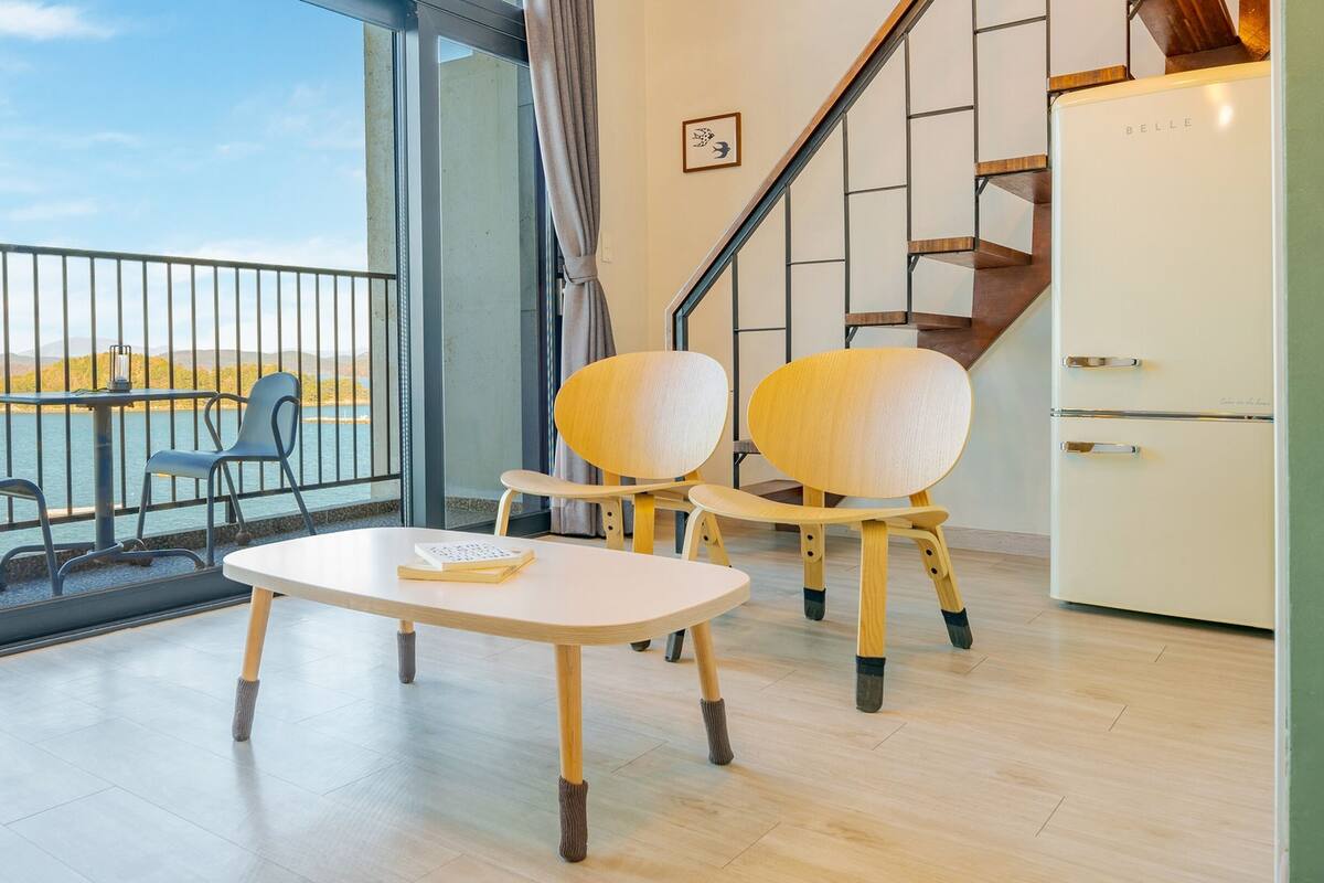 A modern room with a balcony, two wooden chairs, a small table, and a white refrigerator.
