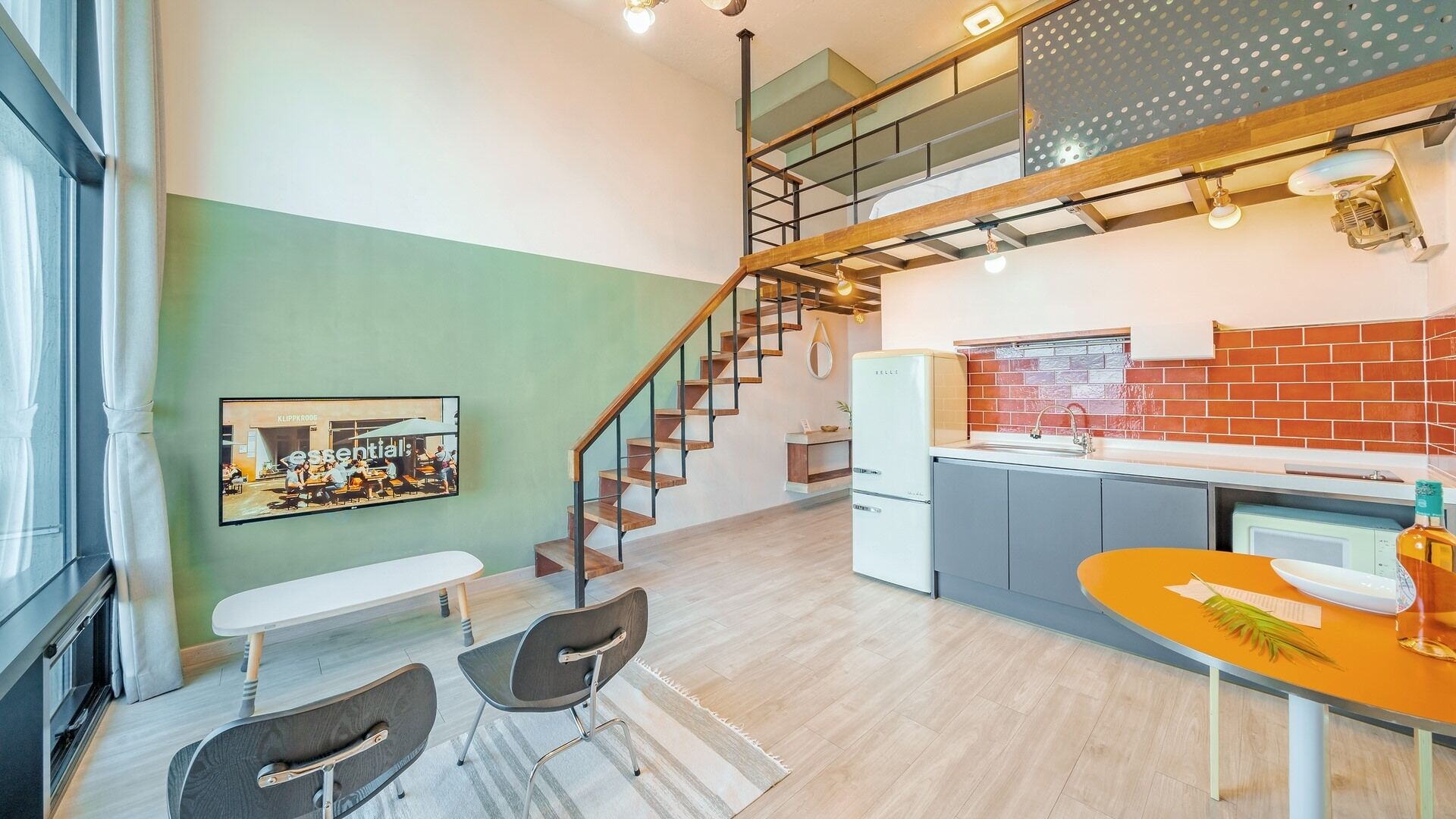A modern kitchen with a brick backsplash, a dining area with a table and chairs, and a staircase leading to an upper level.