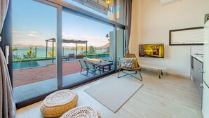 Una habitación moderna con un amplio ventanal corredero que da a una zona de piscina, un televisor de pantalla plana en la pared y una mesa de comedor con sillas.