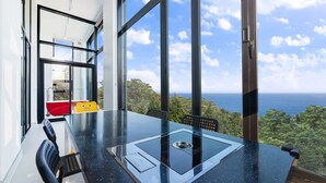 Un espace repas moderne avec une table en verre, des chaises et une vue sur l’océan.