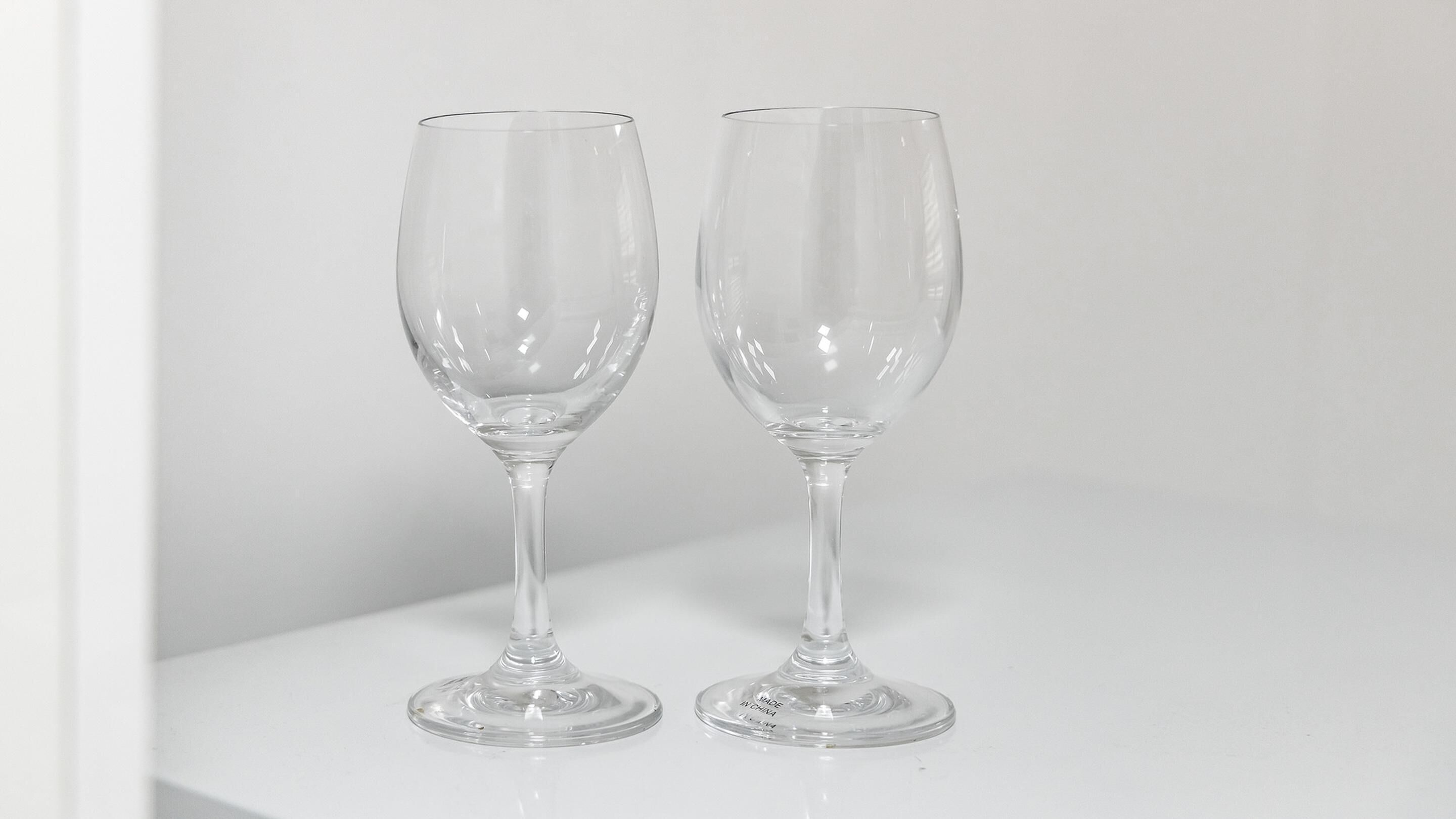 Two clear stemmed wine glasses on a white surface.