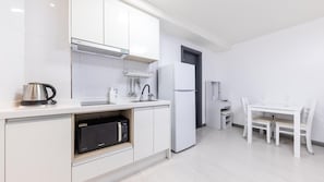 A modern kitchen with white cabinetry, a built-in microwave, a kettle, and a refrigerator. - Yeosu Onueli Pension (Yeosu)