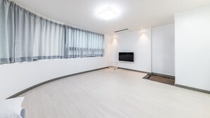 A spacious room with a large window, a flat-screen TV mounted on the wall, and a light-colored wooden floor. - Yeosu Onueli Pension (Yeosu)