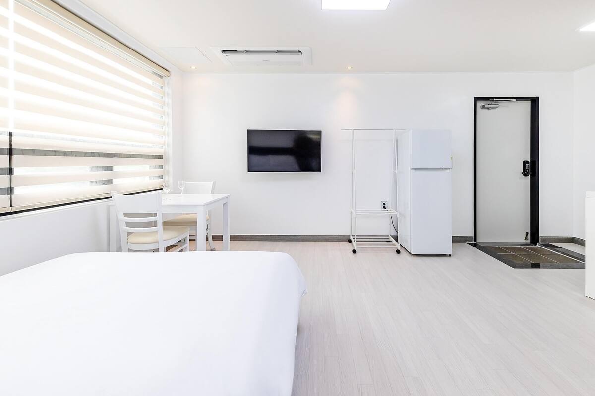 A hotel room with a bed, a desk, a TV, a refrigerator, and a door.