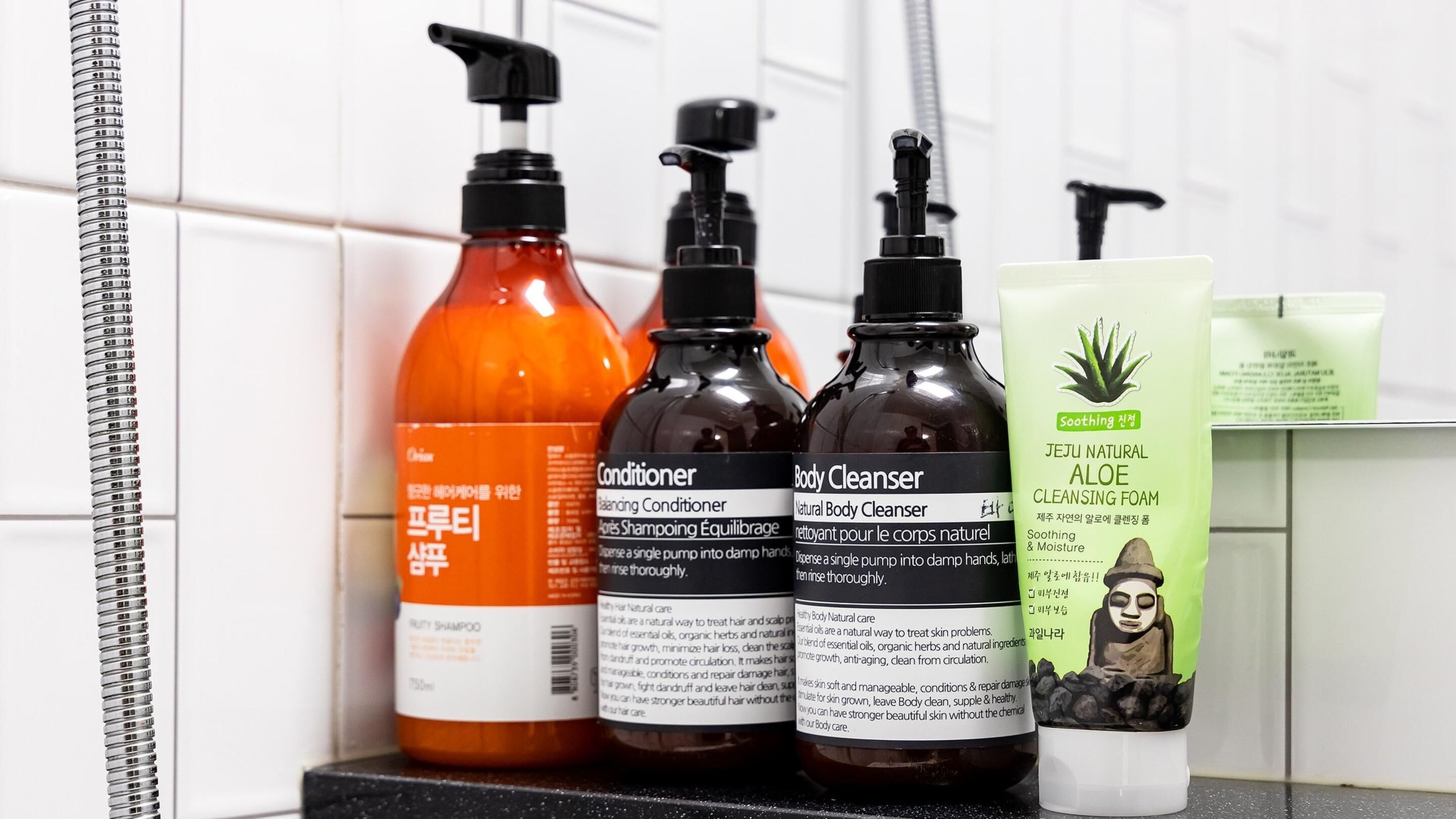 Un estante de baño con tres botellas de productos para el cabello y una caja de espuma limpiadora de aloe vera.