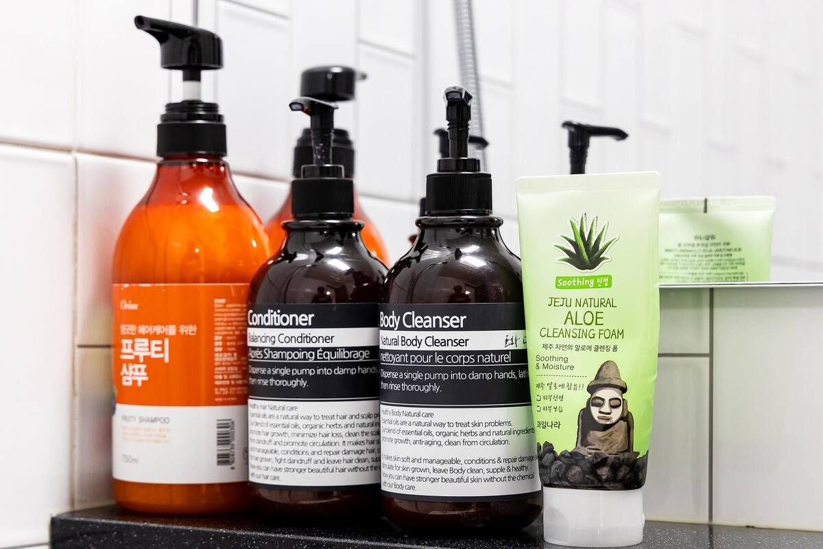 A bathroom shelf with three bottles of hair care products and a box of aloe cleansing foam.