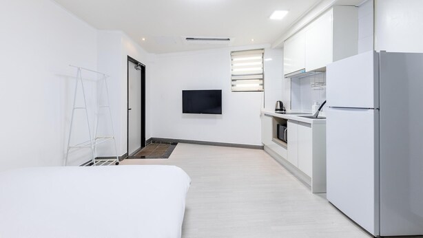 A modern, minimalist hotel room with a bed, a small kitchenette, and a TV mounted on the wall. - Yeosu Onueli Pension (Yeosu)