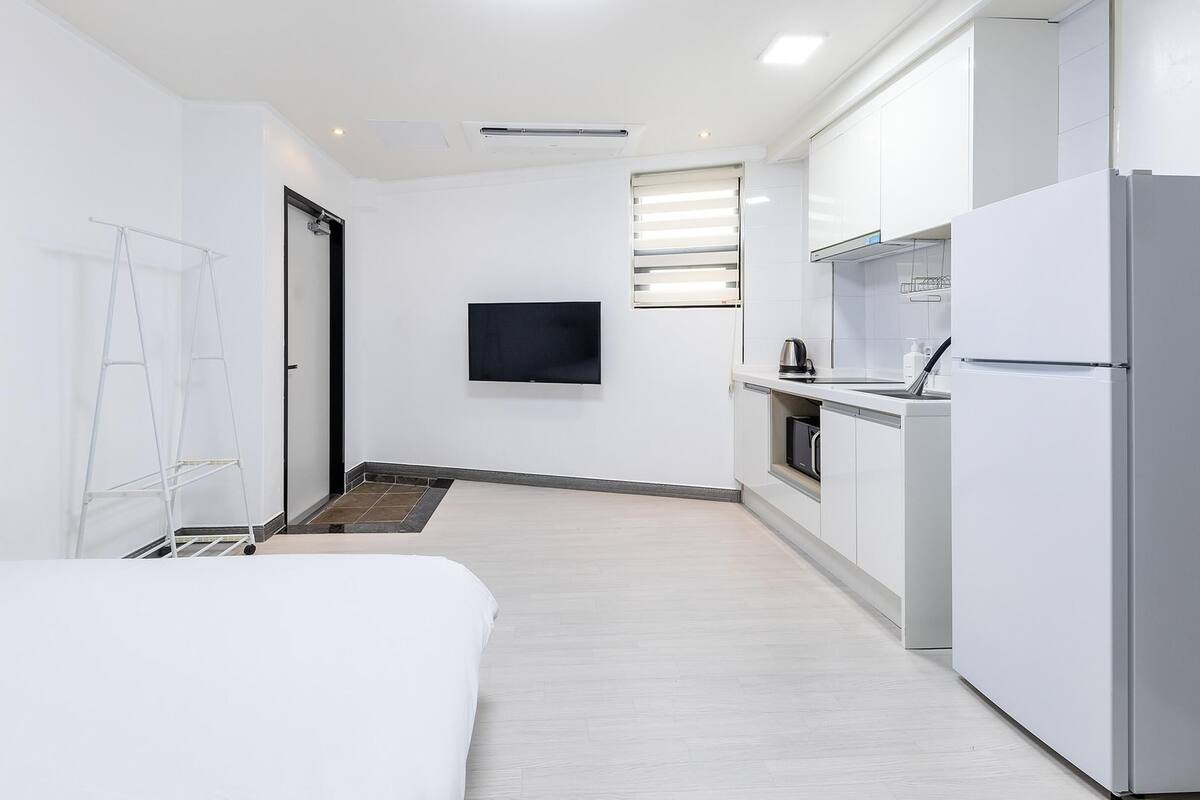 A modern, minimalist hotel room with a bed, a small kitchenette, and a TV mounted on the wall.