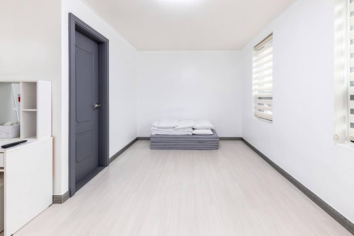 A narrow hallway with a bed, a desk, and a door.