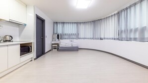 A modern, compact room with a kitchenette, a bed with pillows, a small table, and a window with curtains. - Yeosu Onueli Pension (Yeosu)