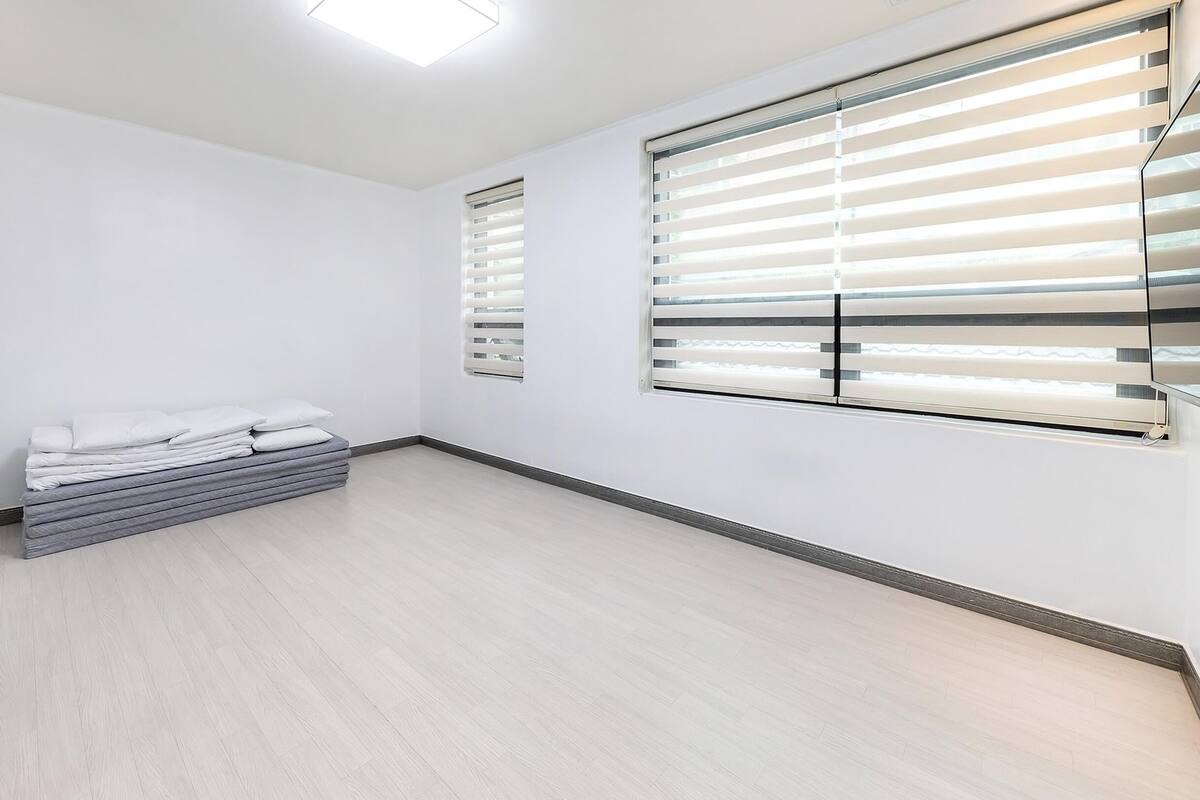 A room with a bed, a small seating area, and large windows with blinds.