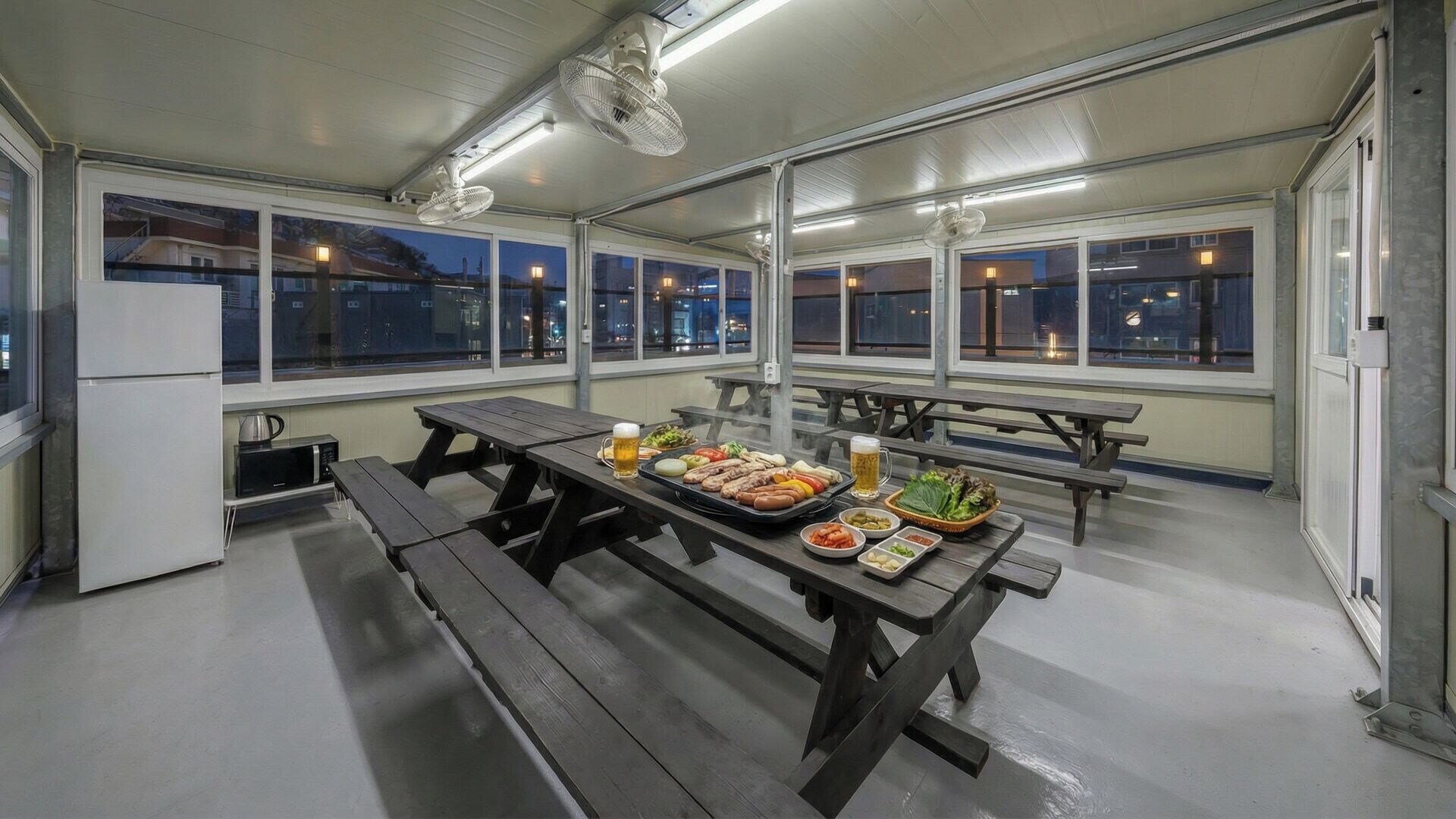 Een eetruimte binnenshuis met tafels, banken en diverse soorten eten.