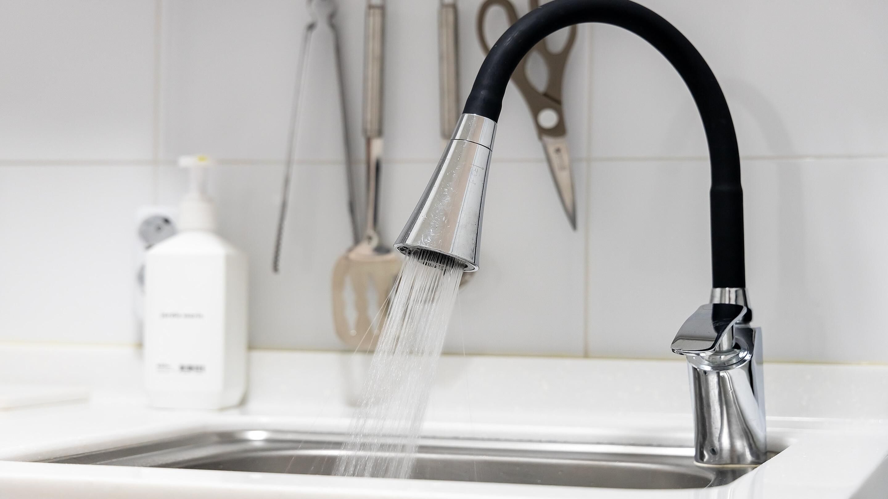A modern kitchen sink with a high-arc faucet, a soap dispenser, and a pair of scissors on the wall.