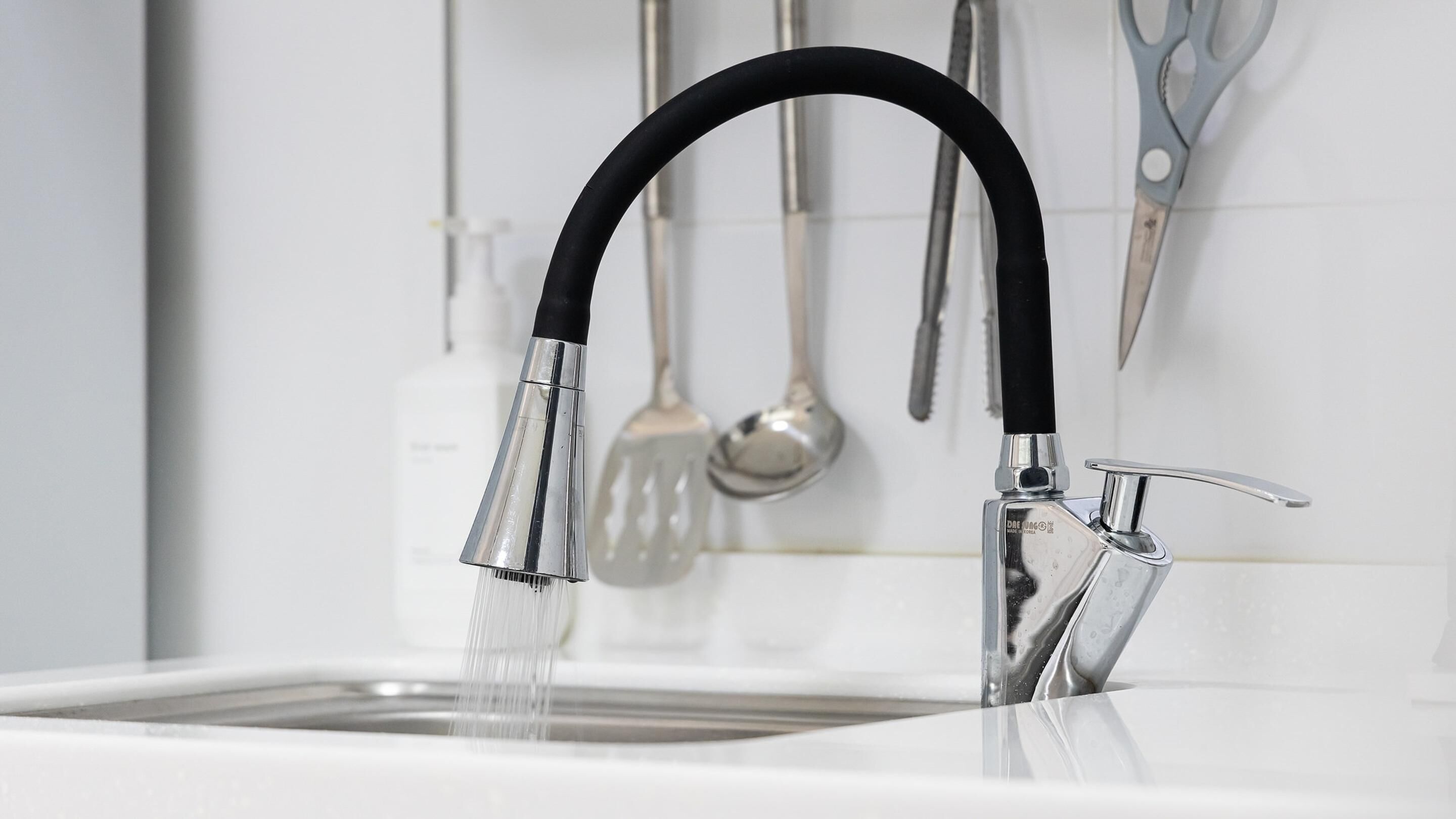 A modern kitchen sink with a black hose faucet and a chrome faucet.