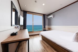 Une chambre d’hôtel avec une grande fenêtre, un lit, un bureau, un miroir et un appareil de climatisation.