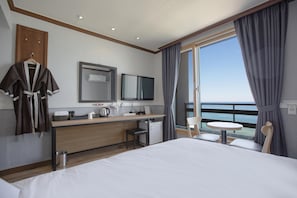 Une chambre d’hôtel avec un lit, un bureau, une chaise, une petite table, un téléviseur et une vue sur la mer.