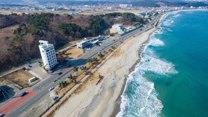 Vista aérea de una zona costera con una carretera, un edificio de techo rojo y una playa.