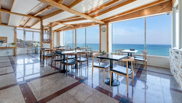 A spacious dining area with large windows overlooking the sea, featuring wooden beams and tiled flooring. - Yangyang Eight (Yangyang)