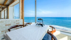 A dining area with a table set for two, overlooking a beach with the ocean and a distant cityscape. - Yangyang Eight (Yangyang)