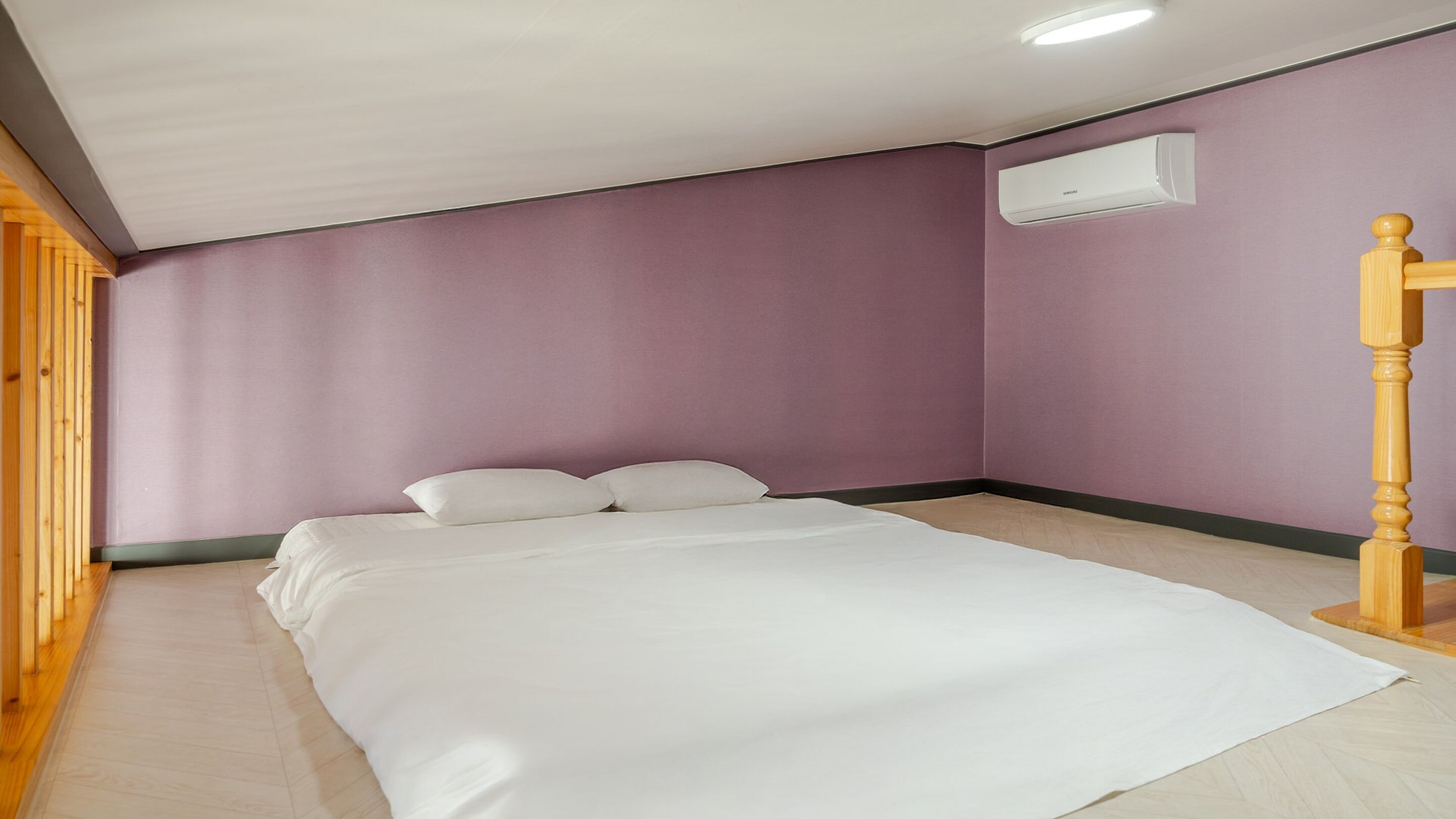 A bedroom with a bed, wooden floor, purple walls, and a ceiling light.