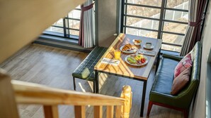 A dining area with a table set for breakfast, a bench, and a view through large windows. - Samcheok Lamer Pension (Samcheok)