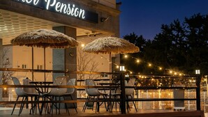 An outdoor seating area with thatched umbrellas and string lights, a sign reading "Pension," and a view of trees and a building in the background. - Samcheok Lamer Pension (Samcheok)