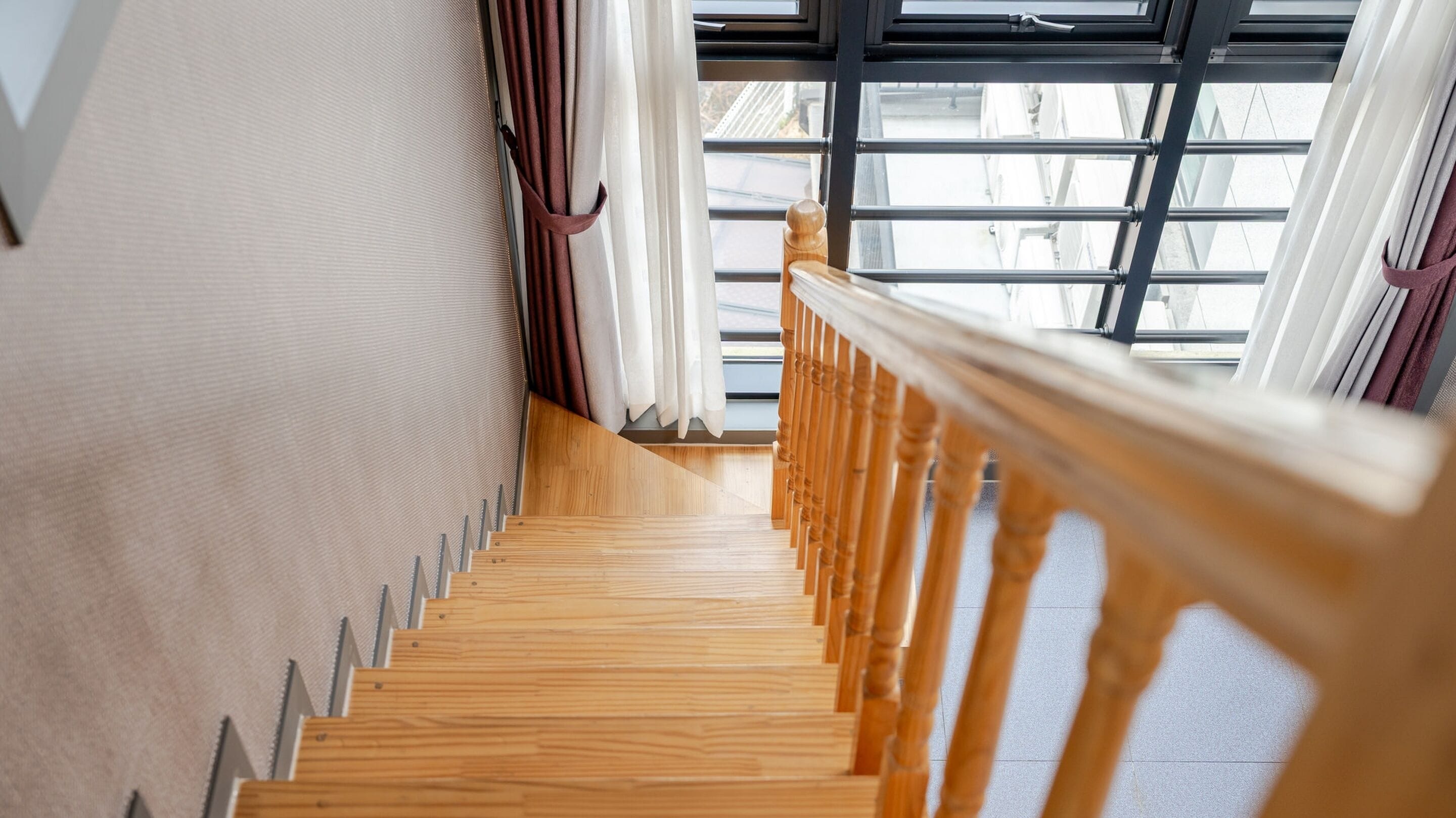 A wooden staircase with a handrail leading to a window with a view of buildings outside.