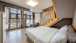 A modern bedroom with a large bed, a wooden staircase, and a view through the glass doors. - Samcheok Lamer Pension (Samcheok)