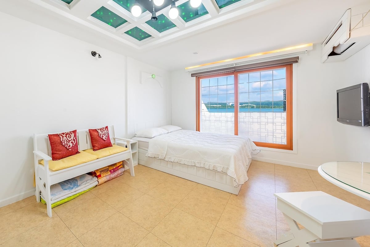 Une chambre à coucher comprenant un lit, une table de chevet, une chaise, un bureau et une fenêtre donnant sur un beau paysage.