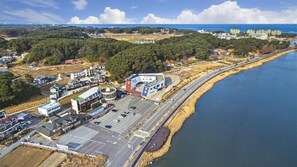 An aerial view of a coastal area with a parking lot, buildings, and a road curving along the shoreline. - Gangneung Five Moon Pension (Gangneung)