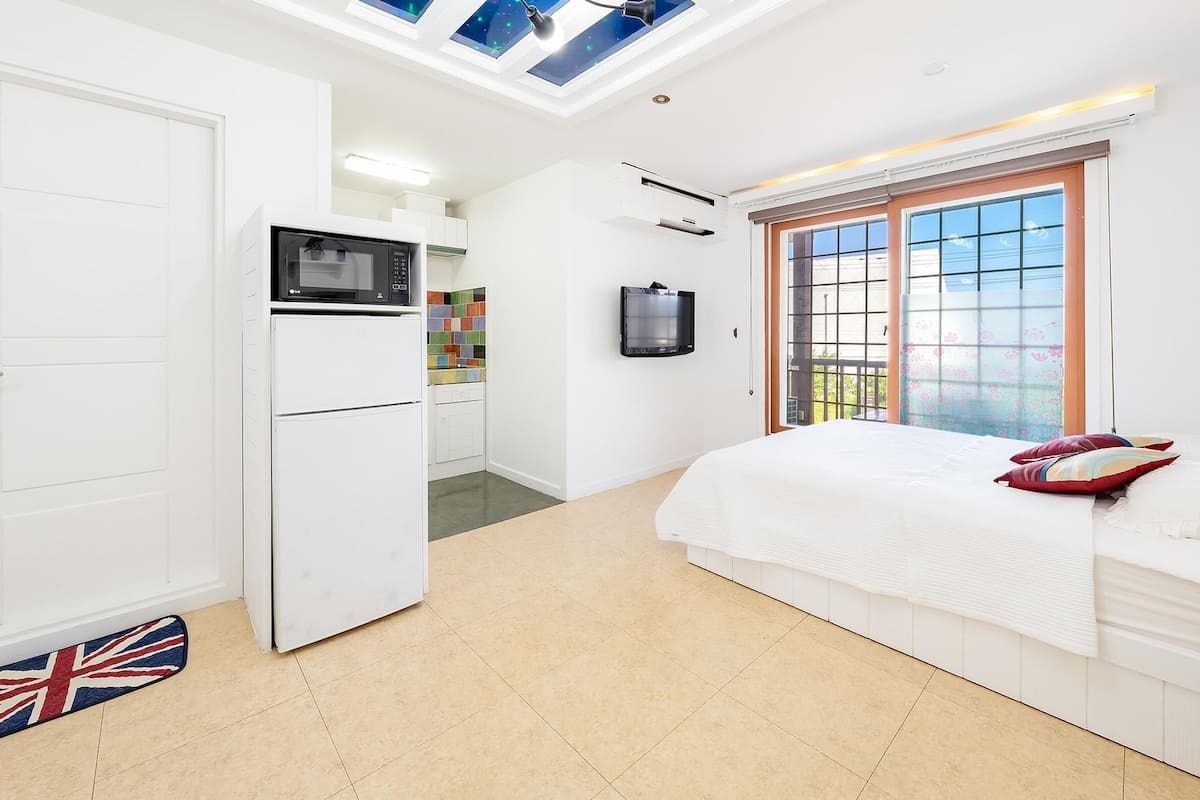 Une chambre avec un lit, une armoire blanche, un petit coin cuisine équipé d’un four à micro-ondes et une fenêtre donnant sur un paysage agréable.