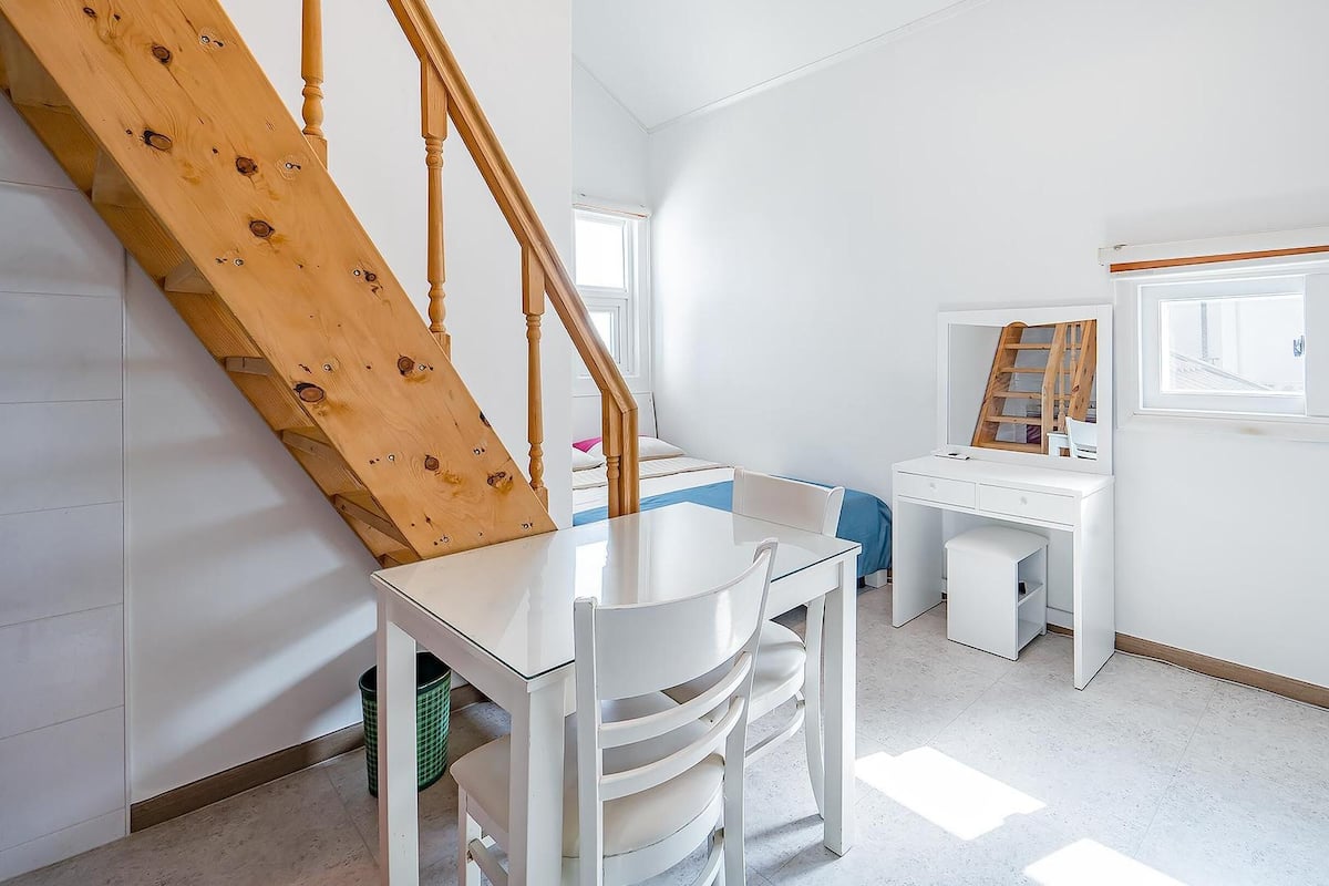 Une chambre d’enfant avec un escalier en bois, un bureau, une chaise et une fenêtre donnant sur un beau paysage.