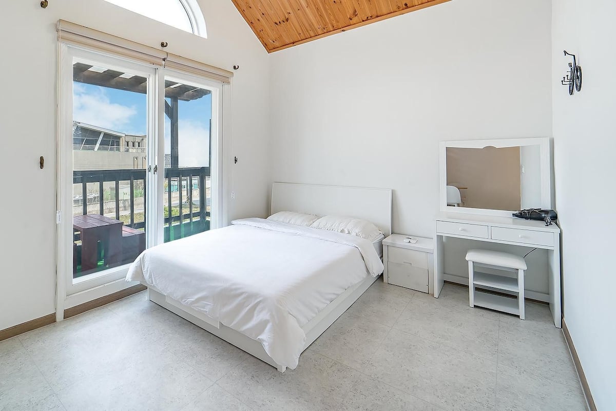 Une chambre à coucher comprenant un lit, un bureau, une chaise, une télévision et un balcon avec vue.