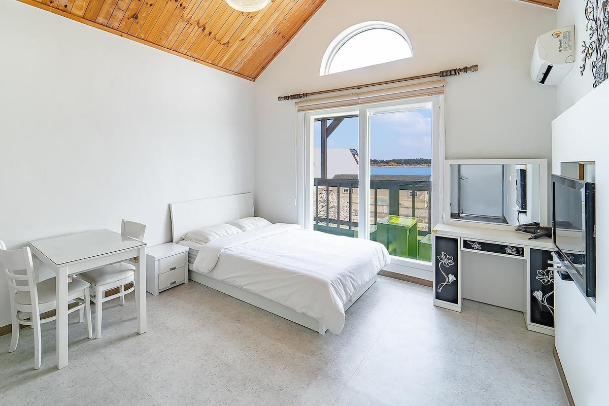 Une chambre à coucher comprenant un lit, un bureau, une chaise, une télévision et un balcon avec vue.