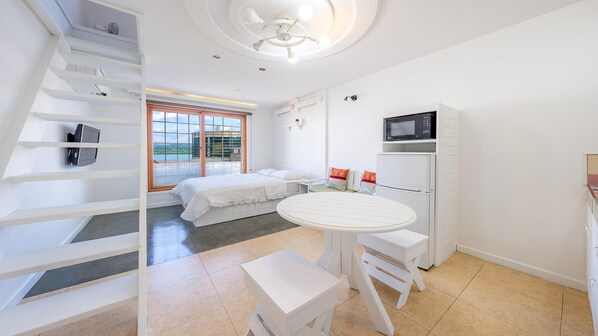 A modern, white-themed bedroom with a bed, a small table, and a chair. There is a window with a view of the outdoors. - Gangneung Five Moon Pension (Gangneung)