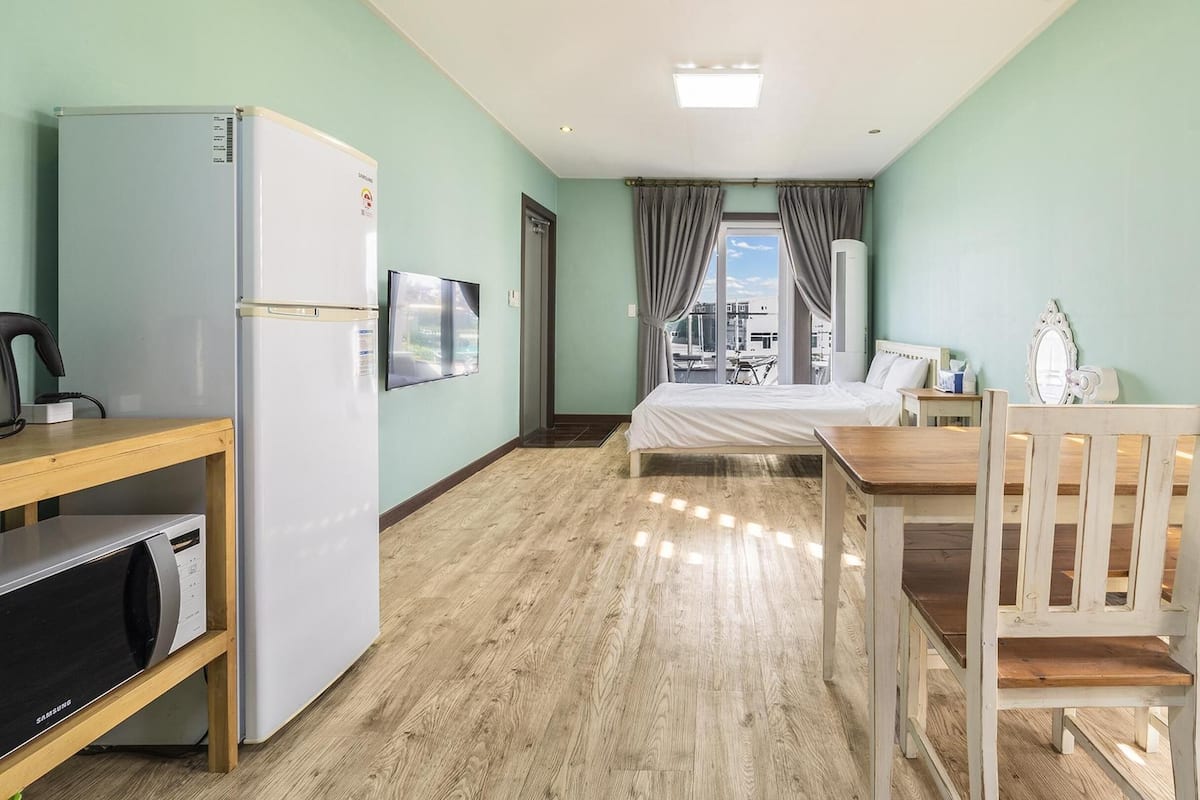 A hotel room with a bed, a desk, a chair, a refrigerator, and a window with curtains.