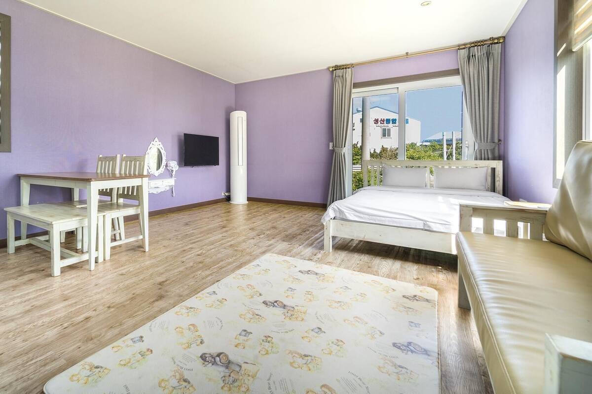 A bedroom with a bed, a desk, a chair, a TV, and a window with curtains.