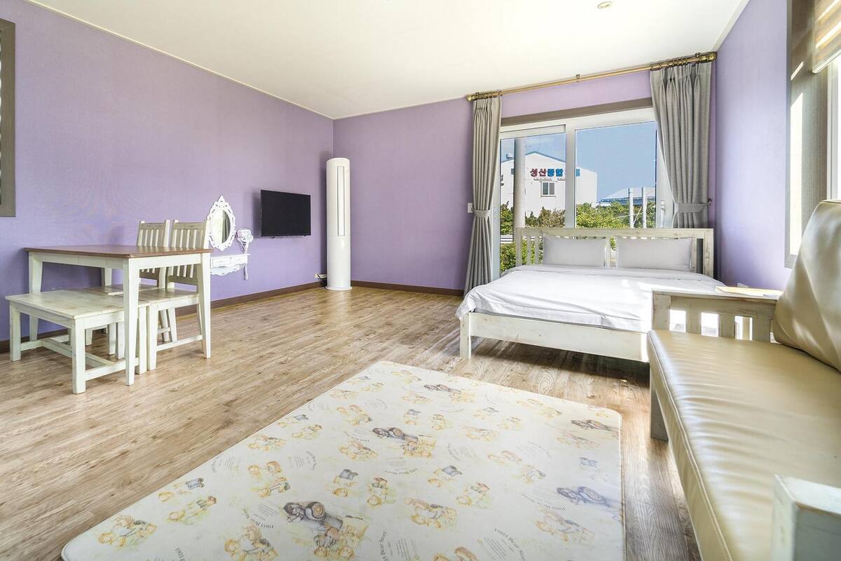 A bedroom with a bed, a desk, a chair, and a window with curtains.
