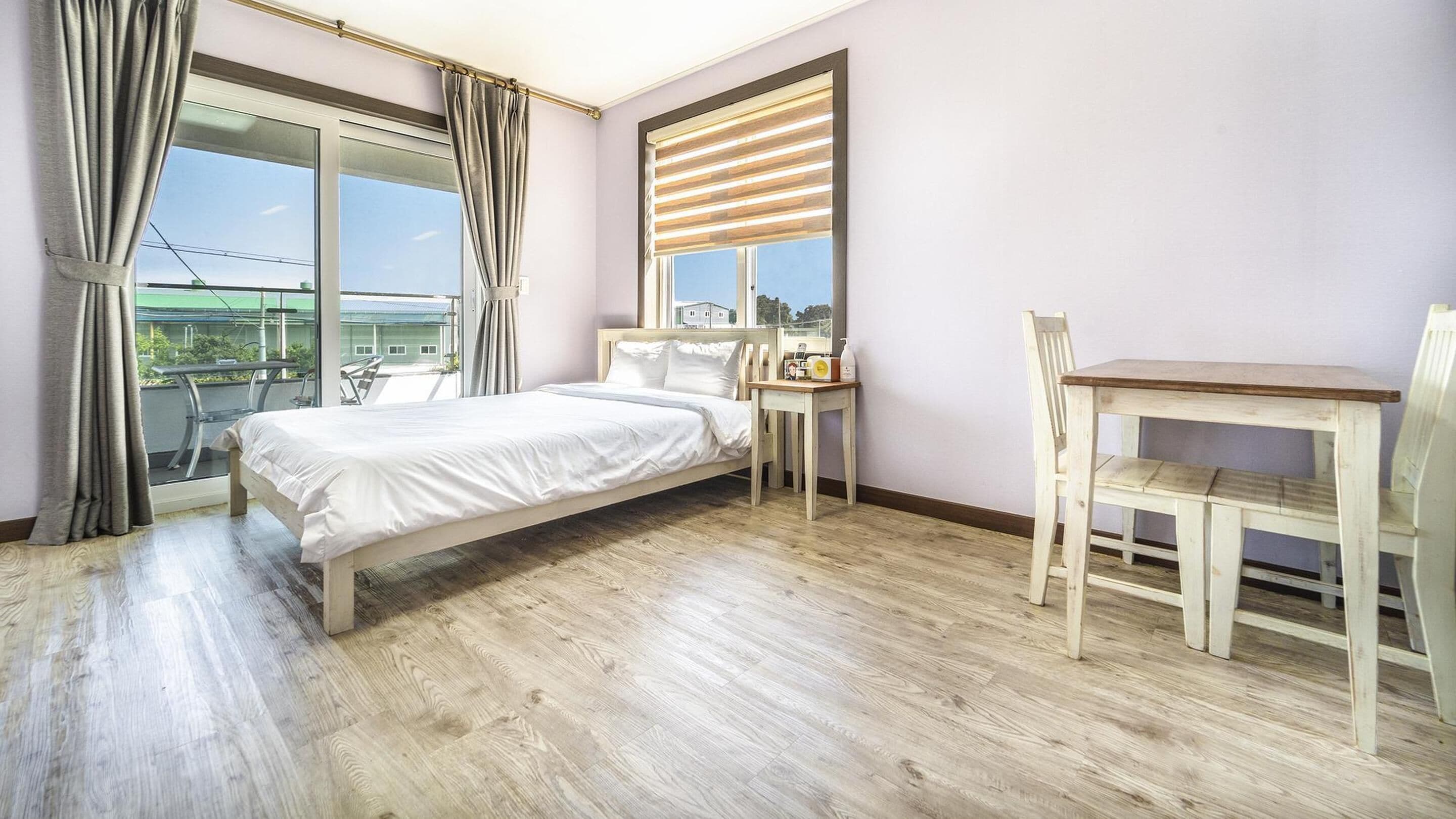 A bedroom with a bed, a desk, and a chair. There is a window with blinds and curtains.