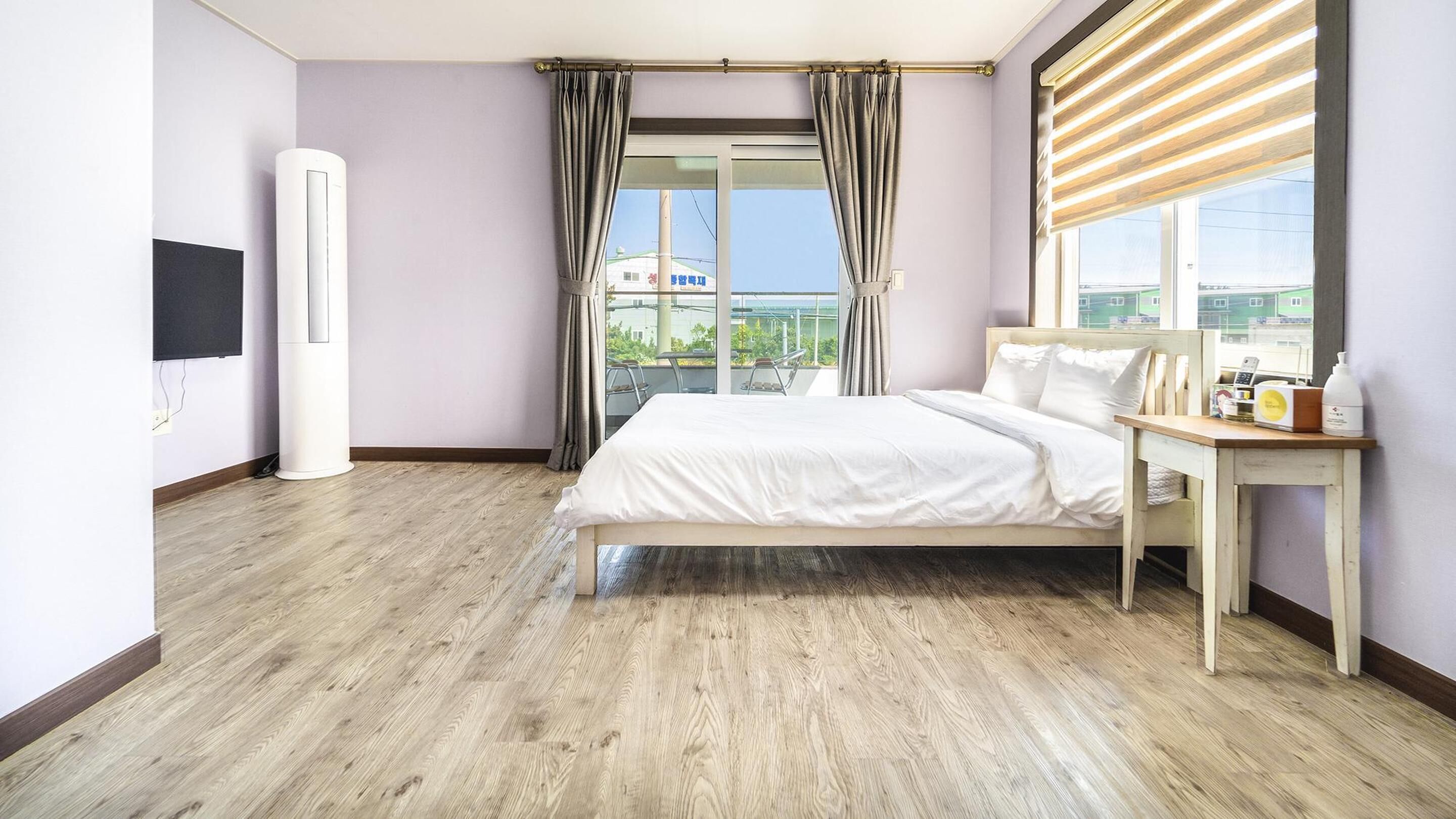 Habitación de hotel moderna con una cama grande, una mesita de noche con artículos de aseo, un televisor y vistas a la ciudad a través de amplios ventanales.