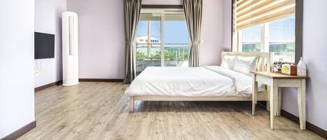 Habitación de hotel moderna con una cama grande, una mesita de noche con artículos de aseo, un televisor y vistas a la ciudad a través de amplios ventanales.