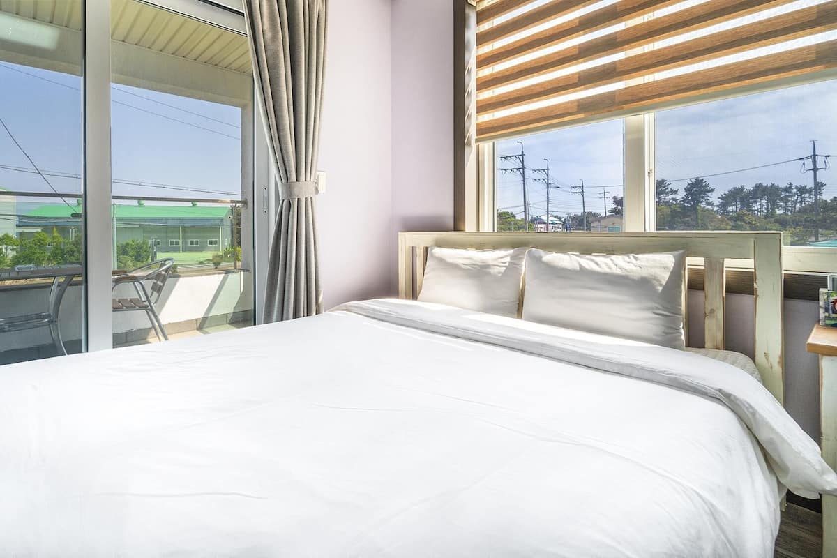 A hotel room with a bed, a view of the outside, and a balcony with chairs.