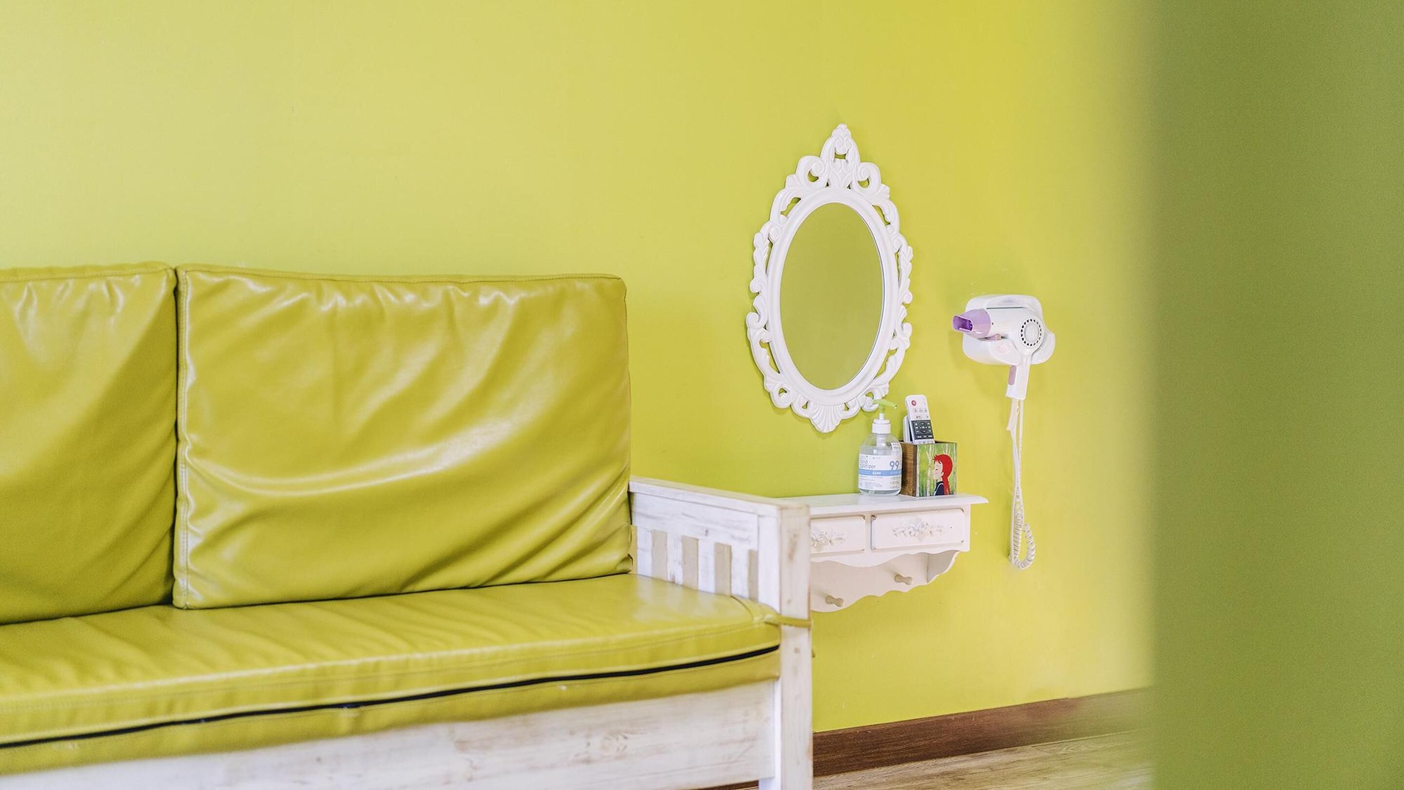 Une chambre avec un mur vert, une coiffeuse blanche avec un miroir, un sèche-cheveux et des articles de toilette.