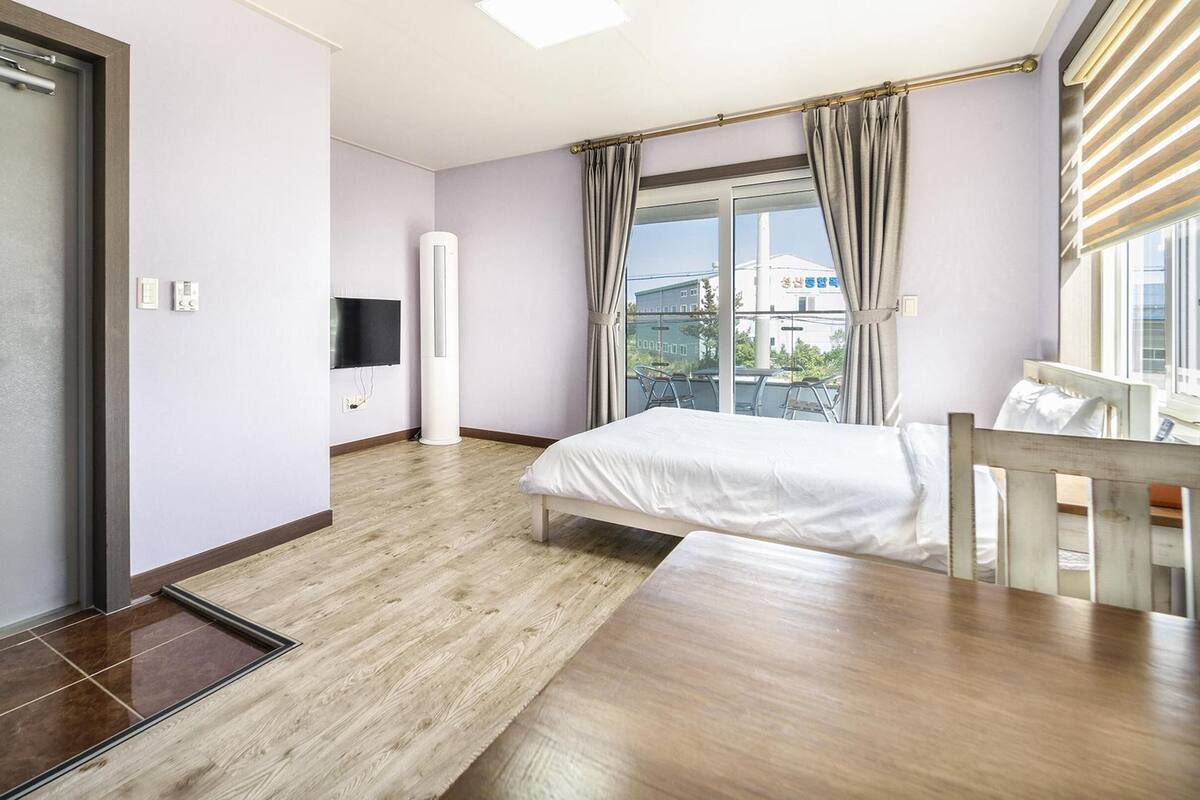 A hotel room with a bed, a desk, a TV, and a window with curtains.