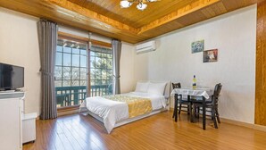 A bedroom with a bed, a desk with a chair, a television, and an air conditioning unit.