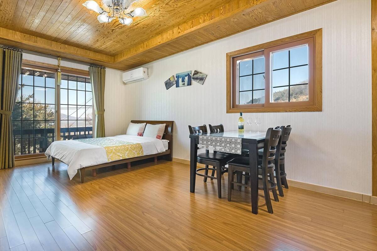 A room with a bed, a dining table with chairs, a TV, and a window with curtains.