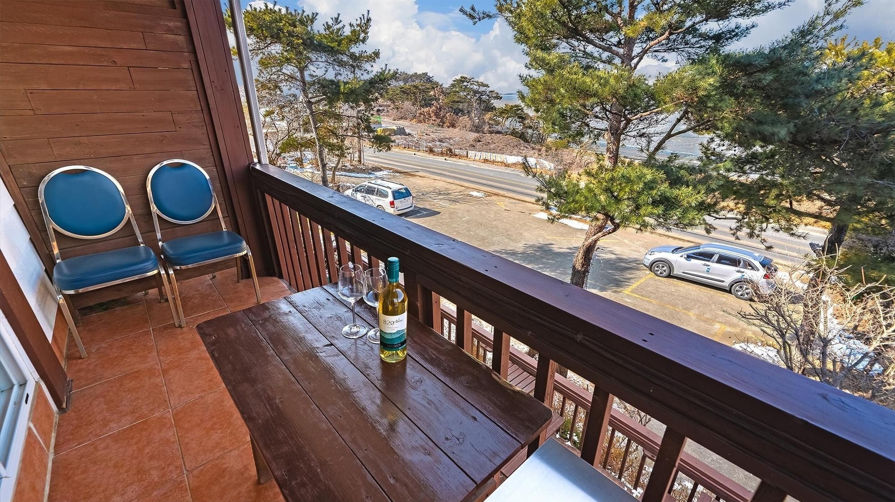 A balcony with a wooden table, two blue chairs, and a bottle of wine.