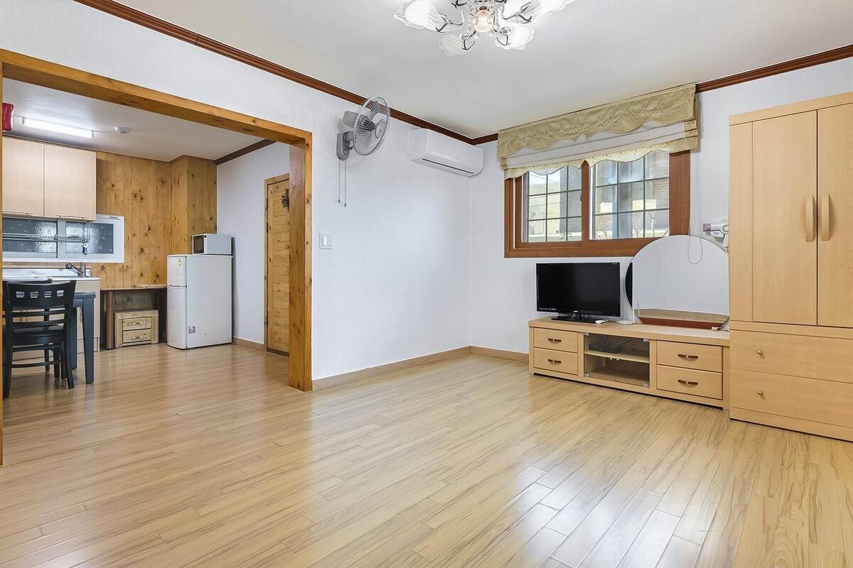 A spacious room with wooden flooring, a kitchenette, a television, and a wardrobe.