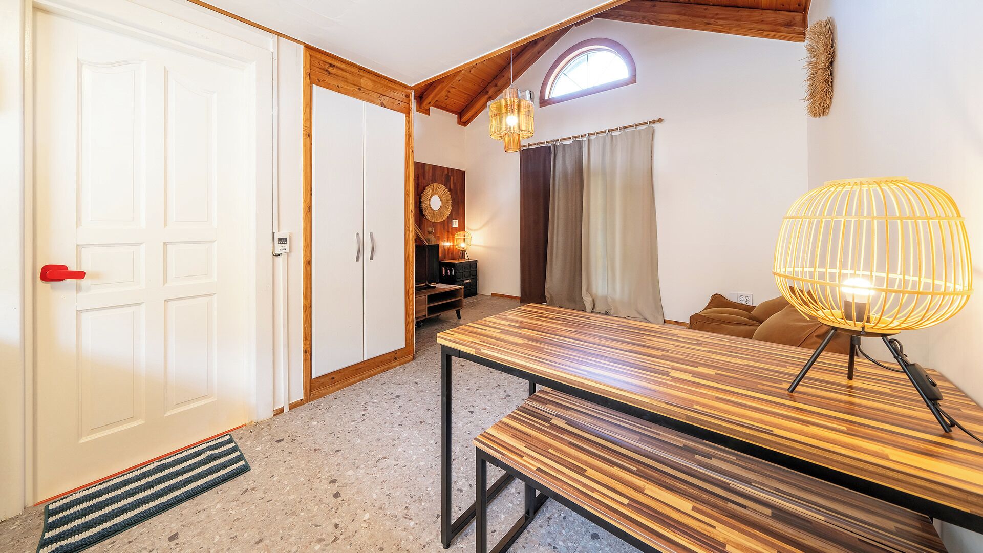 Una habitación con un banco de madera, una mesa, un sofá, una puerta y una ventana con cortinas.