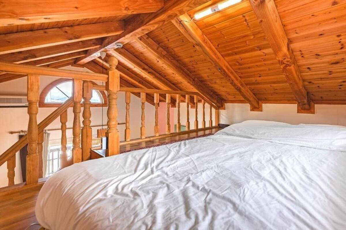 A bedroom with a wooden ceiling, a bed, and a staircase.